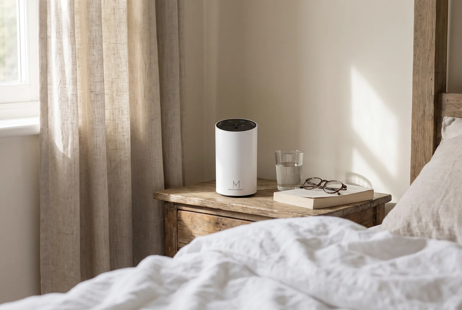 Magnifiscent ScentFlow diffuser in matte white on a bedside table next to a lamp and a paperback